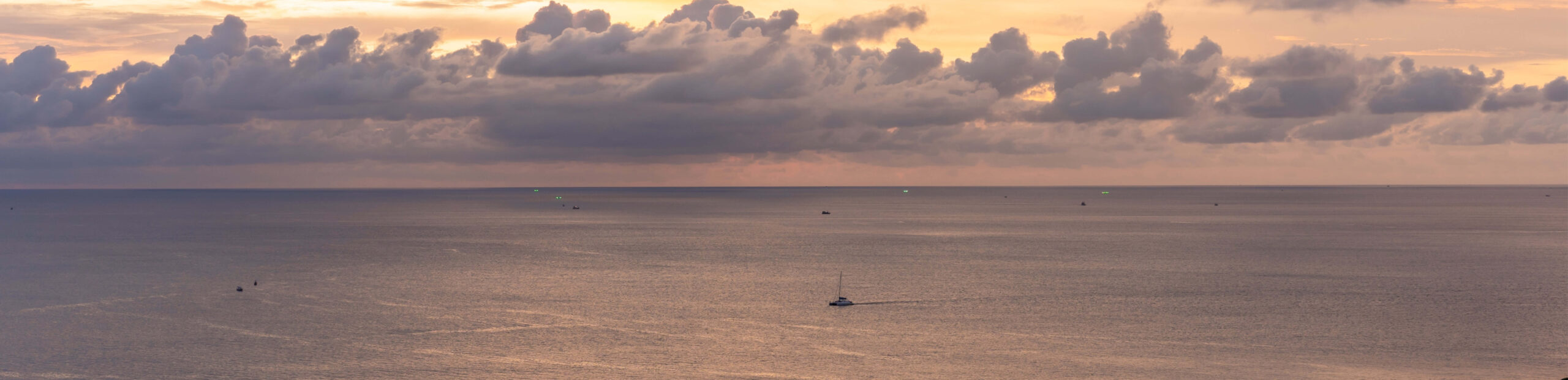 Panoramic seascape at dusk with small vessels on calm water and dramatic clouds, used as a hero image on the tax advisory services page.
